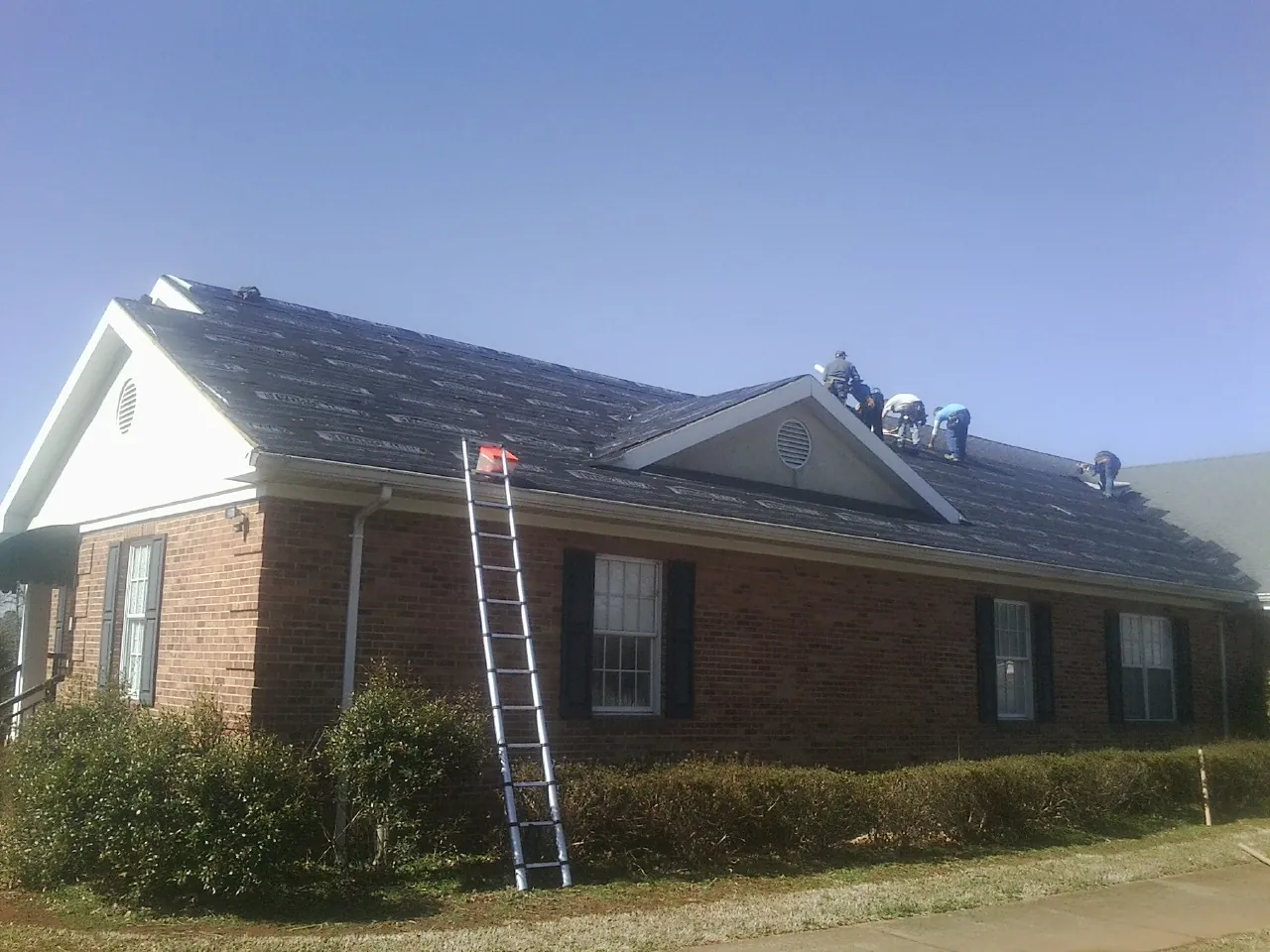 Crew tearing shingles off a brick ranch roof with a ladder set — Emergency Roof Repair work by our crew in Martindale