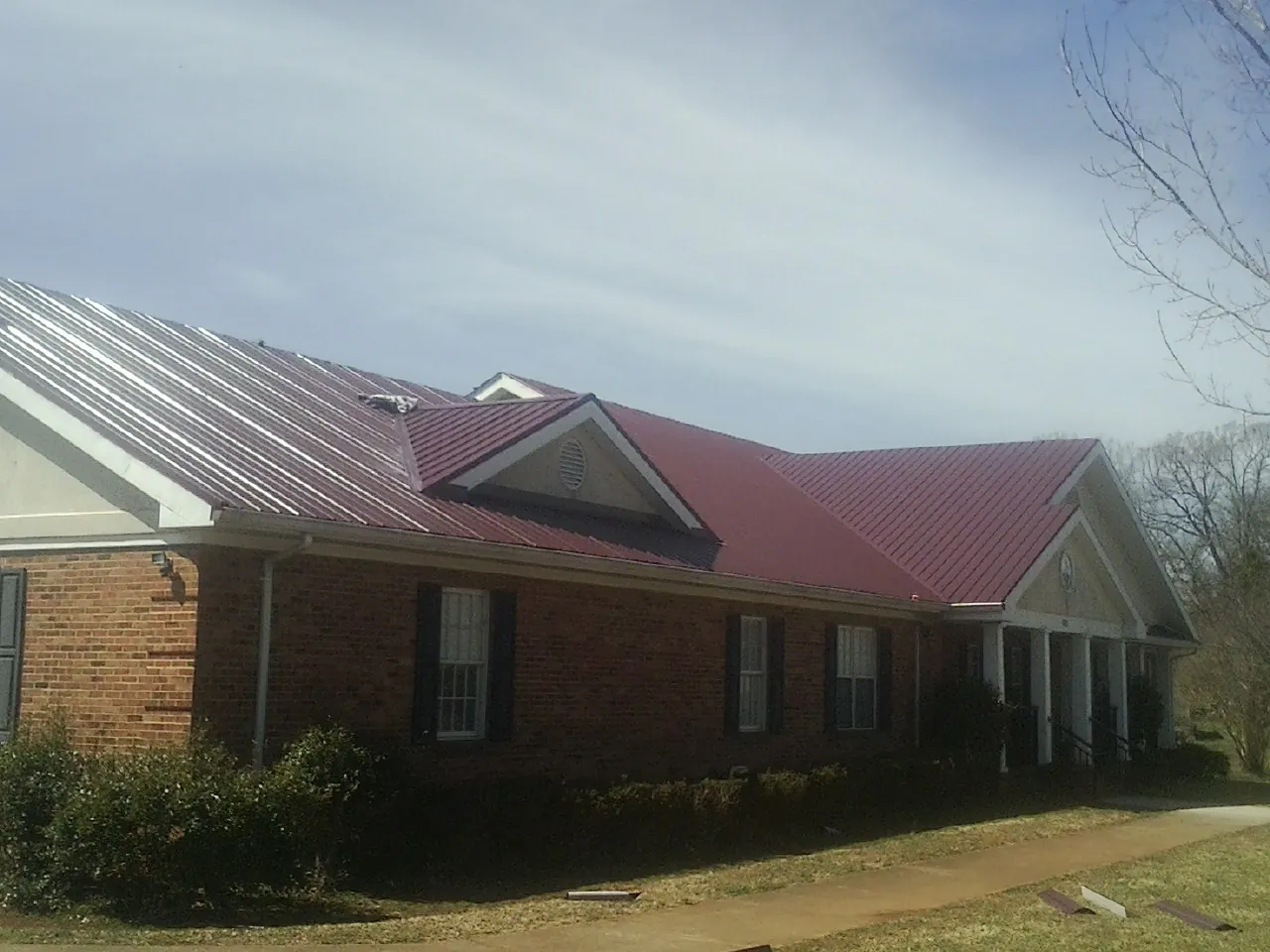 Red metal roof with gabled entries on a long brick building, from a Hail Damage Roof Repair job in Martindale