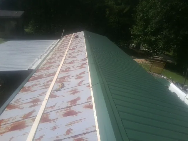 Old rusted panels beside newly installed green metal roofing — Wind Damage Roof Repair by Roofing Brothers in Martindale