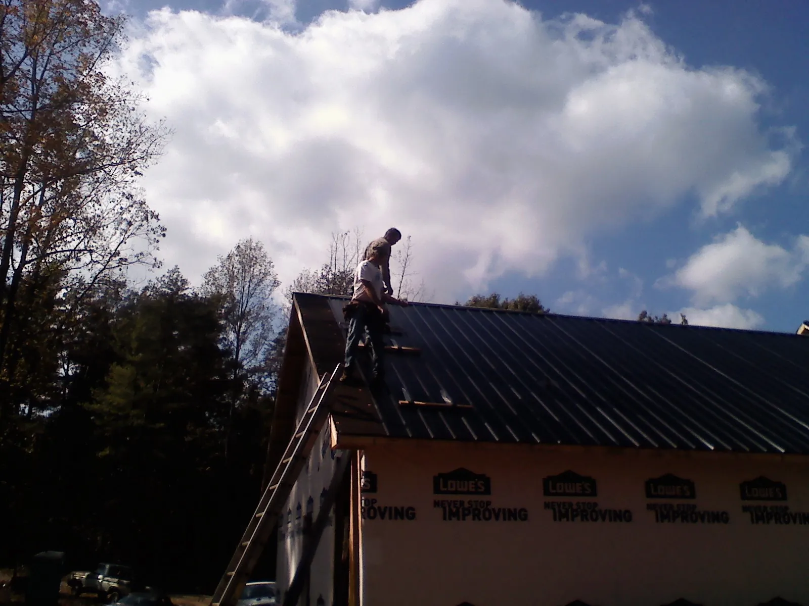 Roofer fastening dark metal panels high against a cloudy sky, from a Roof Inspection job in Martindale