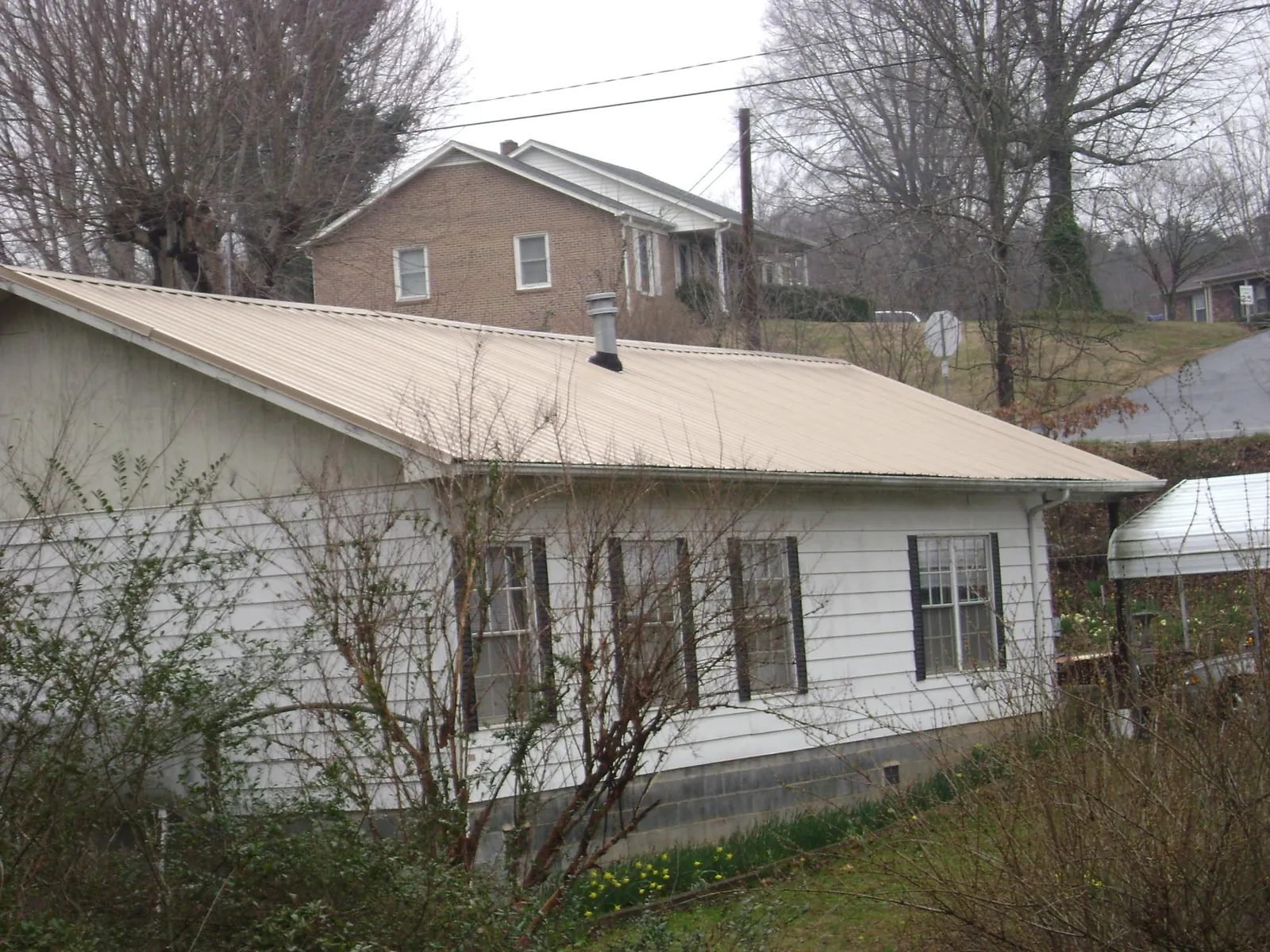 Tan metal roof on a white sided house set into a hillside — Commercial Roofing by Roofing Brothers in Martindale