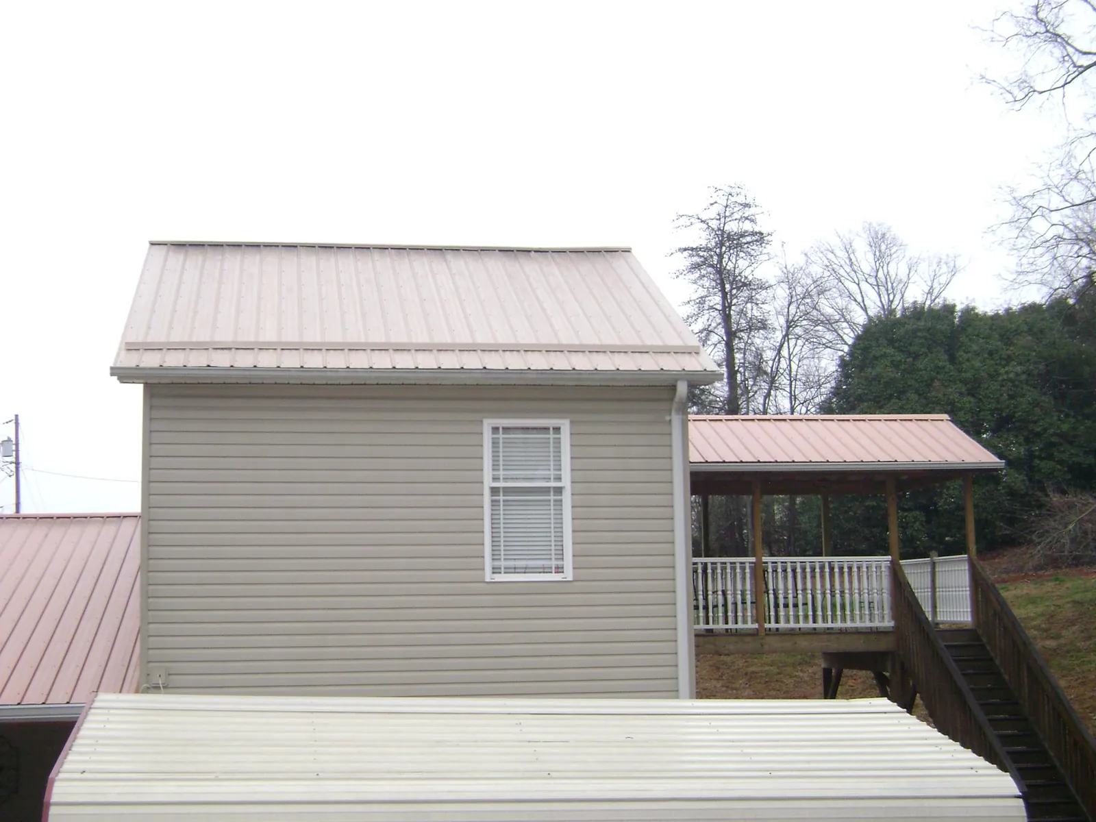 Tan metal roofs on a two story addition and attached porch, from a Roof Replacement job in Martindale